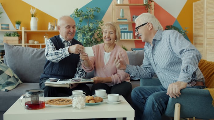 Retired seniors sharing a photograph and laughing together over tea